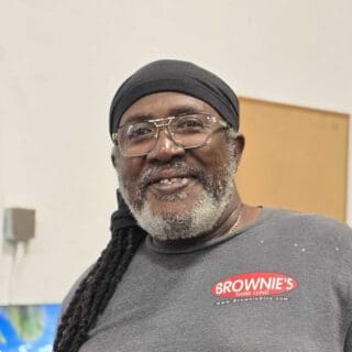 Claude Stuart, smiling technician at Brownie's THIRD LUNG™, wearing a branded shirt, showcasing expertise in shipping and customer service.